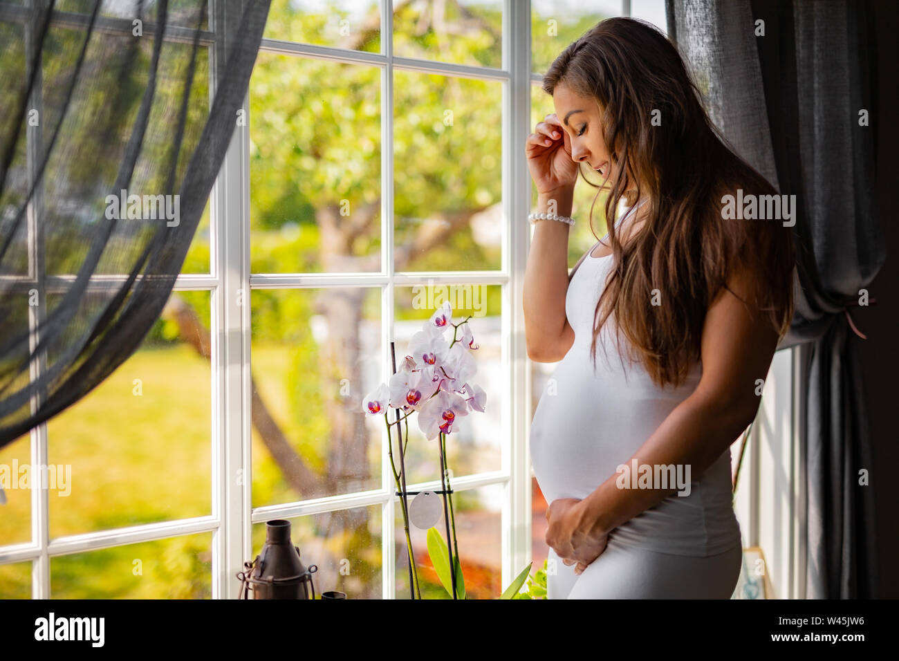 Träumen schwangere Frau schauen aus dem Fenster und ihren Bauch berühren. Stockfoto