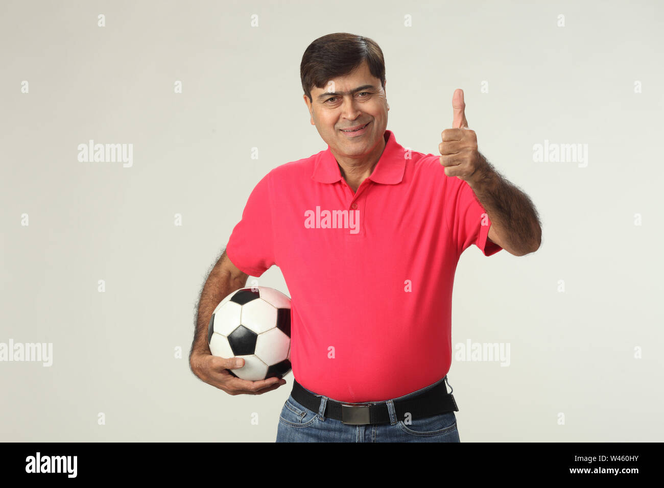 Porträt eines Mannes, der einen Fußball hält und zeigt Daumen hoch Stockfoto