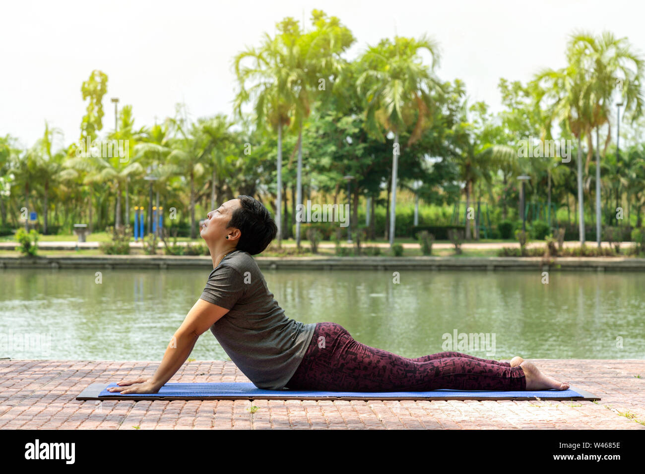 Gesunde asiatische Frau mittleren Alters tun Bhujangasana (Kobra) Yoga im Stadtpark am Morgen dar. gesund und Lifestyle Konzept. Stockfoto