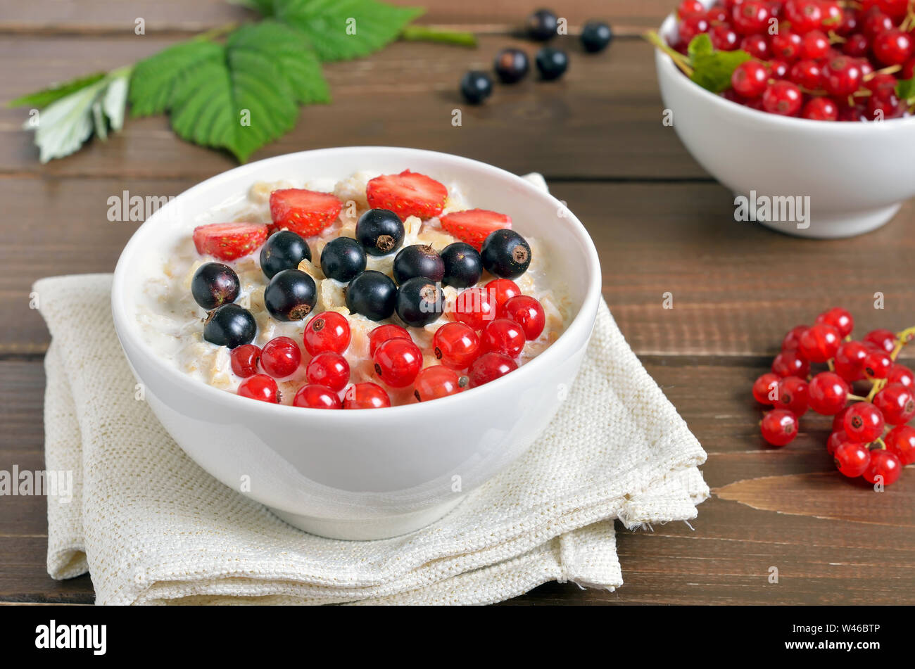 Haferflocken Porridge mit roten und schwarzen Johannisbeeren und Erdbeeren auf hölzernen Tisch Stockfoto