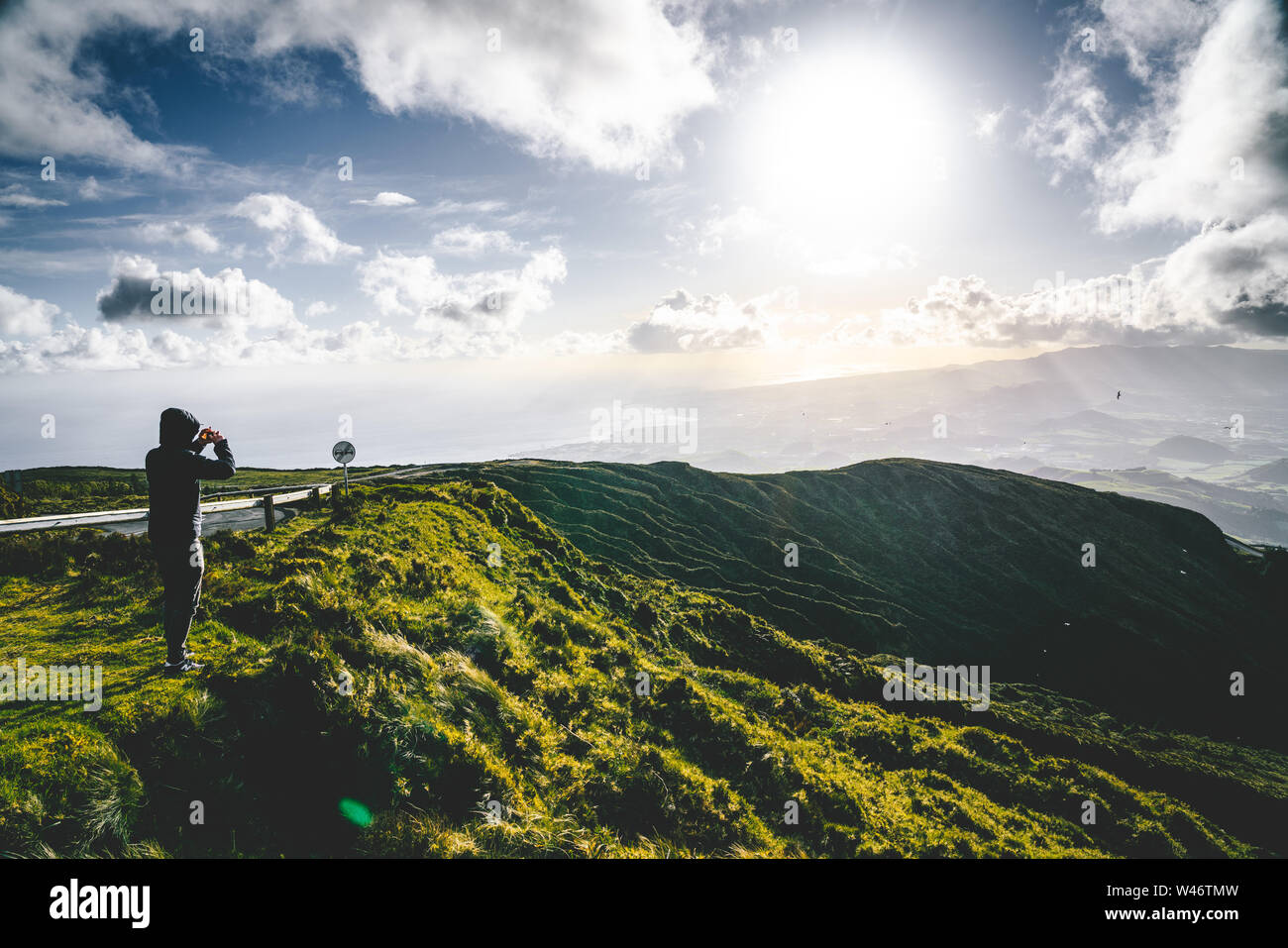 Junger Mann touristische mit Blick auf den wunderschönen Panoramablick von Lagoa do Fogo, See von Feuer, in Sao Miguel, Azoren, Portugal. Sonnigen Tag mit blauem Himmel Stockfoto