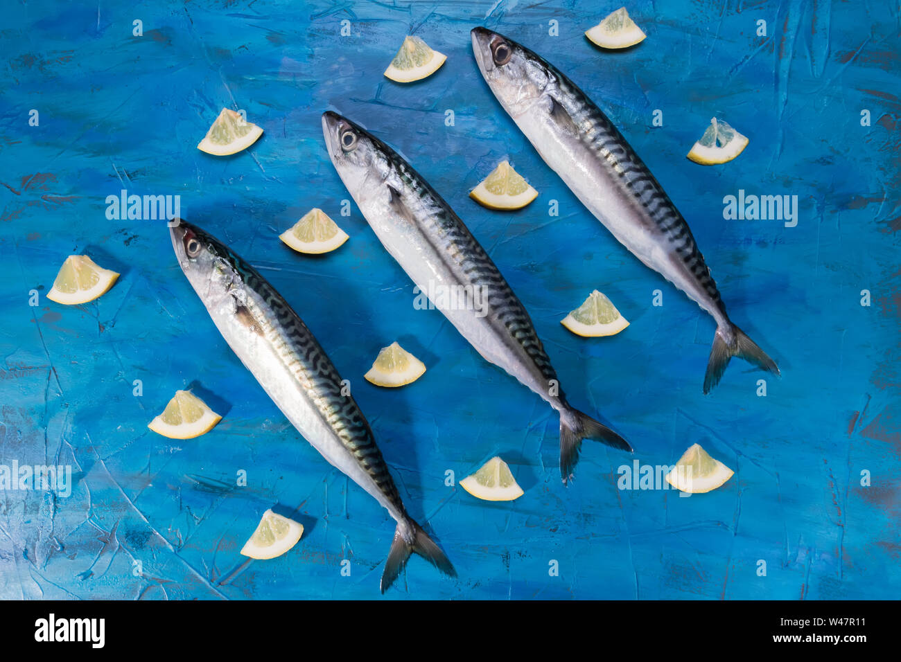 Drei rohe frische Makrele Fisch mit Zitrone auf auf einem blauen Meer Hintergrund, Ansicht von oben. Fisch gefangen im Ionischen Meer Stockfoto