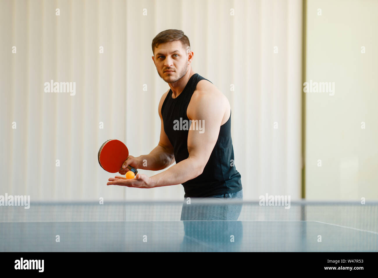 Mann mit Ping pong Schläger vorbereiten, einen Ball zu schlagen, Training im Innenbereich. Männliche Person in Sportbekleidung, Training im Tischtennis club Stockfoto