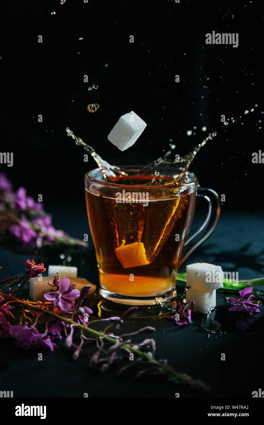 Glas Tasse braunen schwarzen heißen süßen Tee mit Blasen und Spritzer aus geworfen lösen Stück Zucker und zwei Stücke von weißem Zucker. Blühende Sally Stockfoto