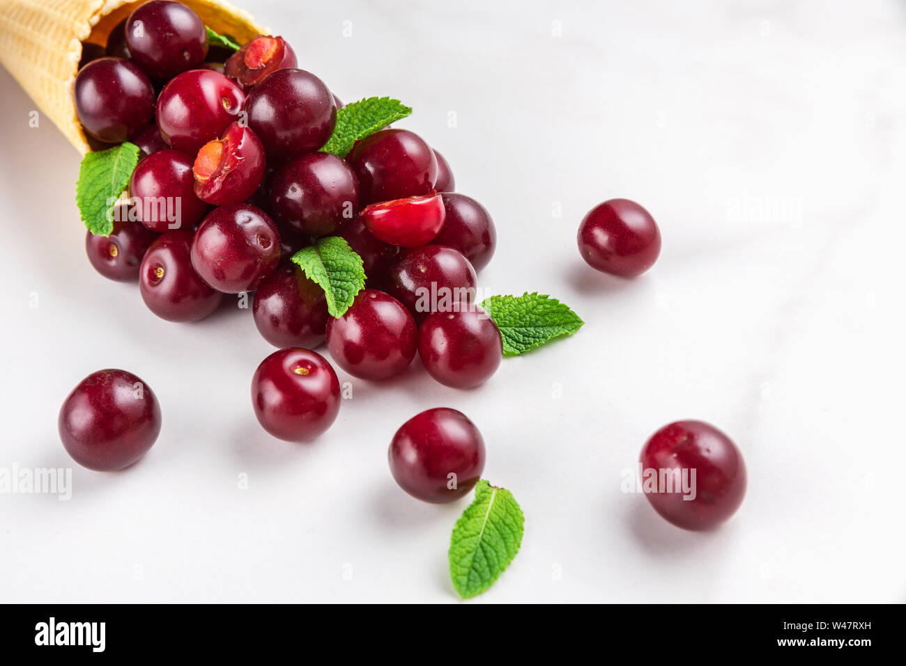 Cherry Beeren mit Minze in Waffel Eiswaffel auf weißem Hintergrund. Sommer essen Konzept. Nach oben Schließen Stockfoto