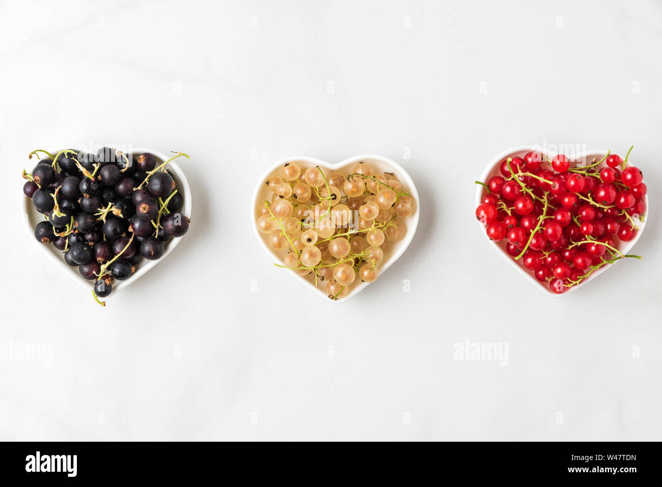 Vielzahl von johannisbeere Beeren Schwarz, Rot und Weiß in Herzform Schüsseln auf weißem Hintergrund. Sommer essen Konzept. Flach. top View Stockfoto