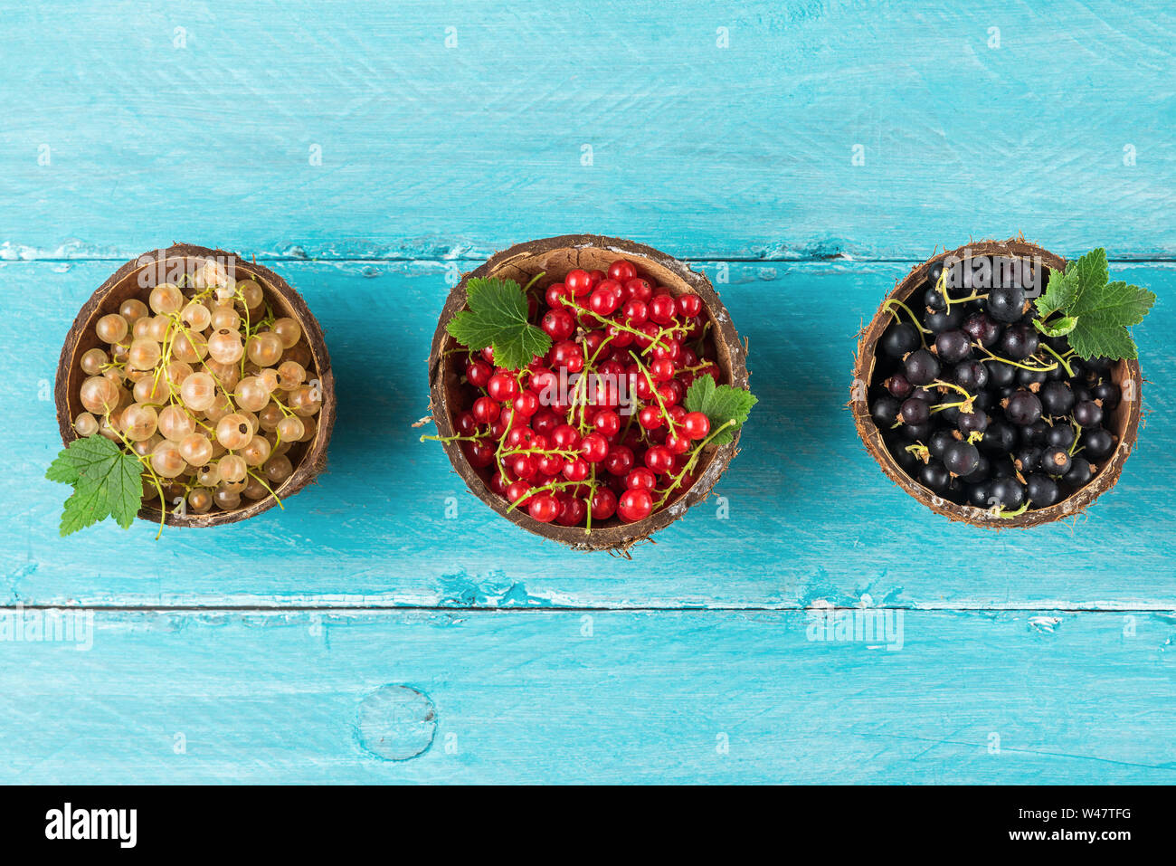 Mischung aus johannisbeere Beeren Schwarz, Rot und Weiß in einem Schalen auf Blau Holz- Hintergrund. Sommer essen Konzept. Flach. top View Stockfoto