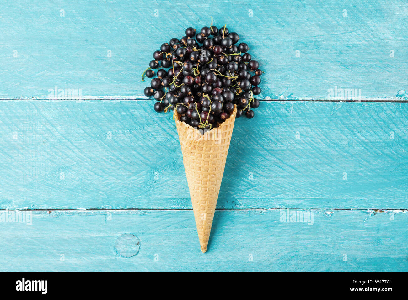Schwarze Johannisbeere Beeren in der Waffel Eiswaffel auf Blau Holz- Hintergrund. Kreative Sommer essen Konzept. Flach. top View Stockfoto