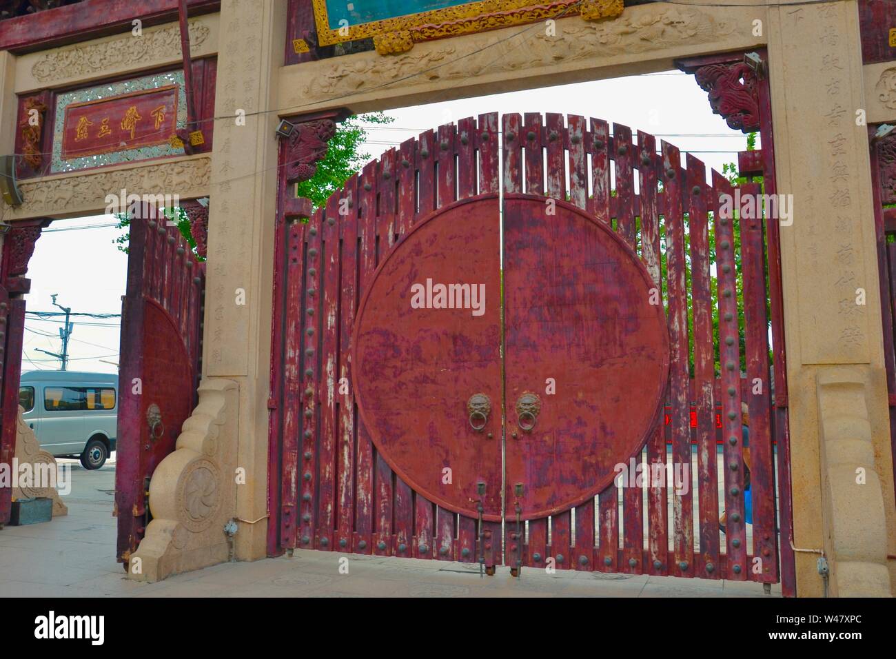 Traditionelle hölzerne Tore am Eingang zu einem chinesischen Tempel. Red Planken und runde Funktion mit verzierten Metall Klopfer, durch Mauerwerk umgeben Stockfoto