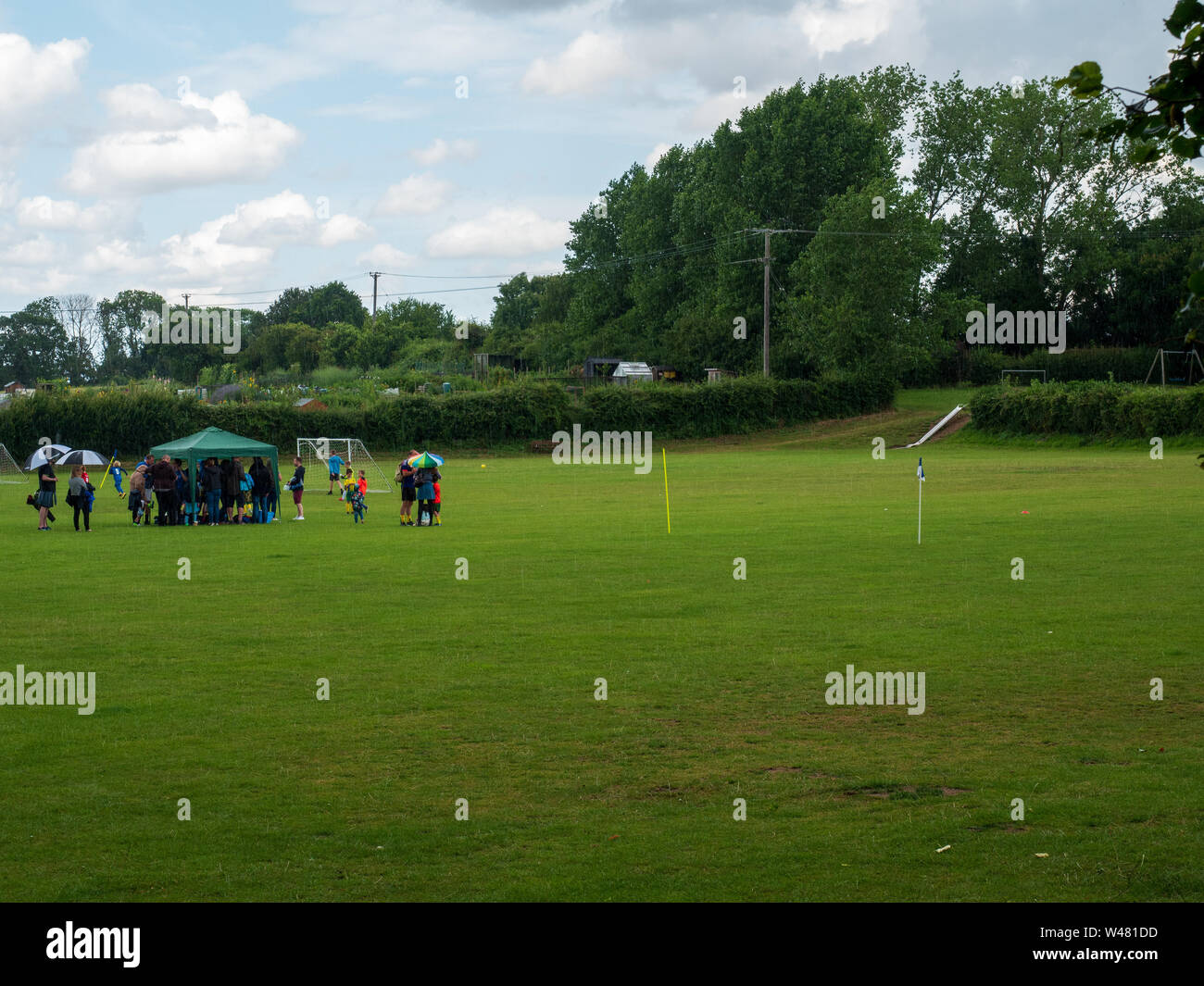 Die Fußballer und ihre Familien nehmen Zuflucht vor einem Sommerregen auf der Stoke Heilig Kreuz Spielen der Felder Stockfoto