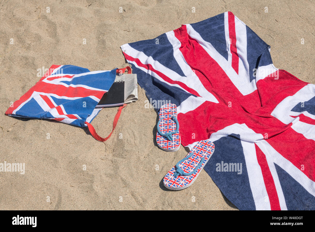 Union Jack Strandhandtuch und Flip-Flops am Sandstrand. Für 2021 Aufenthalte in Großbritannien, Urlaub zu Hause, Aufenthalt in Cornwall, Badeurlaub, Flip-Flop-Schuhe Stockfoto