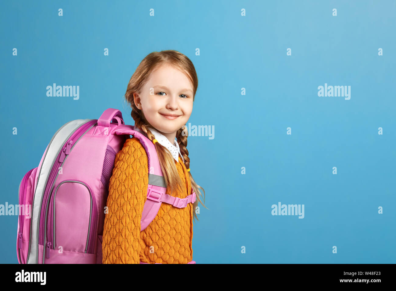 Porträt von einem kleinen Mädchen Schülerin mit einem Rucksack auf blauem Hintergrund. Zurück zu Schule. Der Begriff der Bildung. Stockfoto