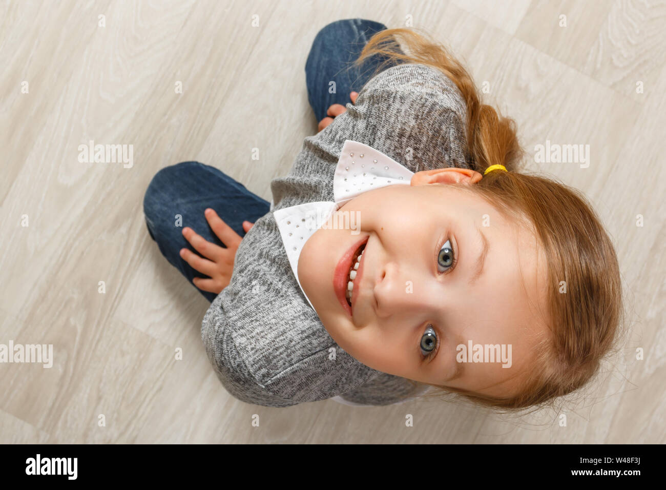 Blick von oben auf ein Kind sitzt auf dem Boden. Das kleine Mädchen hob ihren Kopf hoch und Blick in die Kamera. Stockfoto