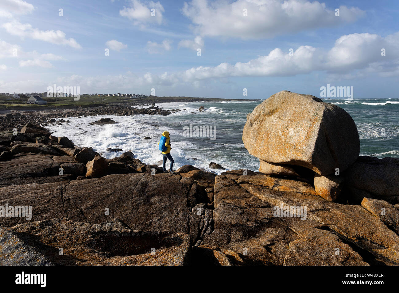 Frau in gelber Jacke stehend auf Granit Felsen beobachten große Wellen aus dem Atlantik auf schroffe Küstenlandschaft in der Bretagne, Frankreich Stockfoto