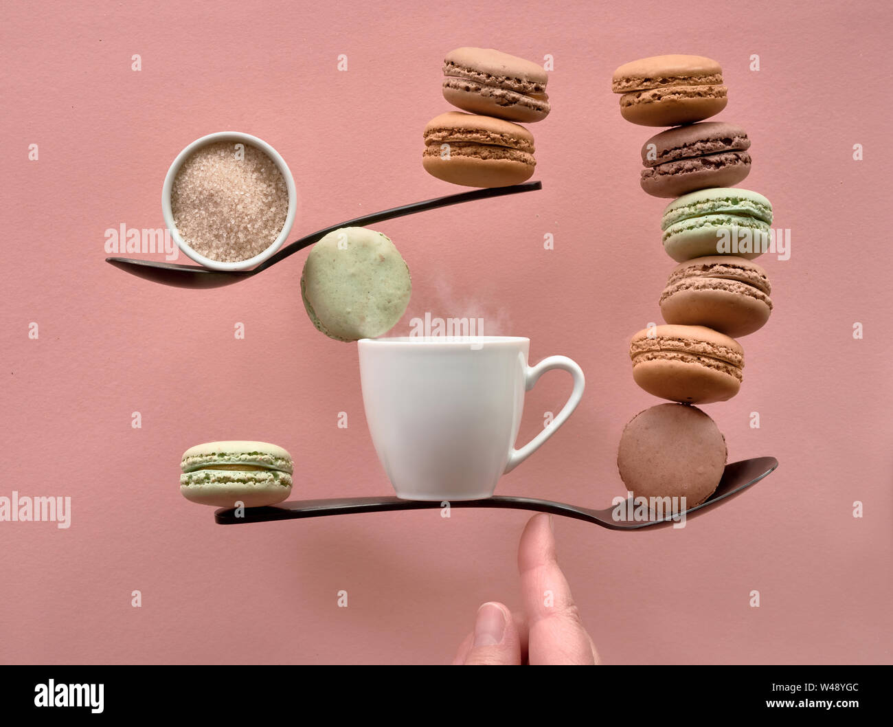 Perfekte Balance Konzept noch Leben auf der Coral Farbe Papier Hintergrund. Balancing Tasse Kaffee, Zucker und macarons auf einem Finger. Stockfoto