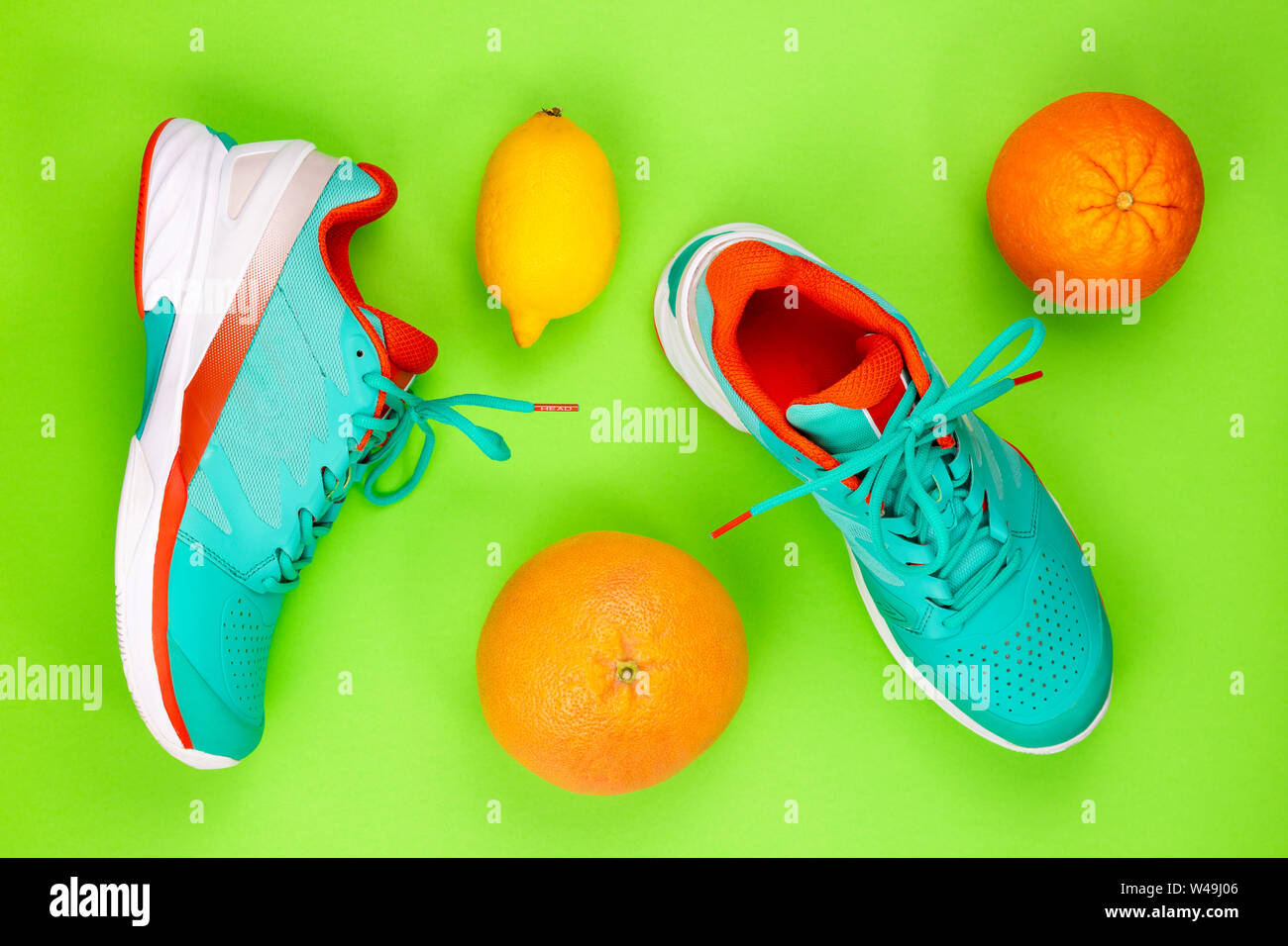 Rot, hellblau, weiß, Paar neue Tennisschuhe im Studio Schuß über Grüner Hintergrund mit Orangen und Zitronen. Direkt von oben. Stockfoto