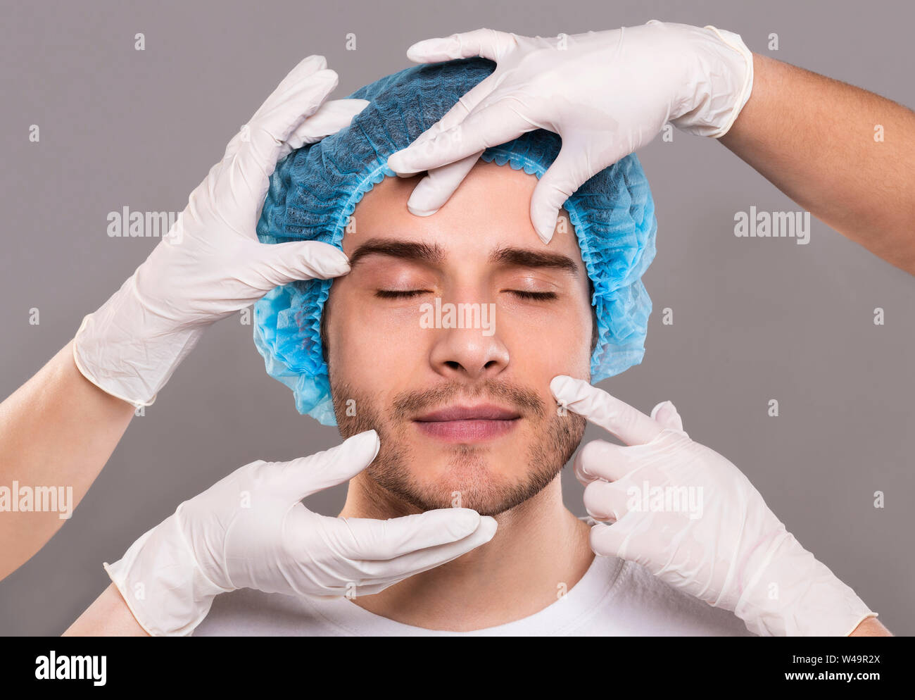 Doctor's Hände in Handschuhen prüfen Gesicht des jungen Mannes Stockfoto