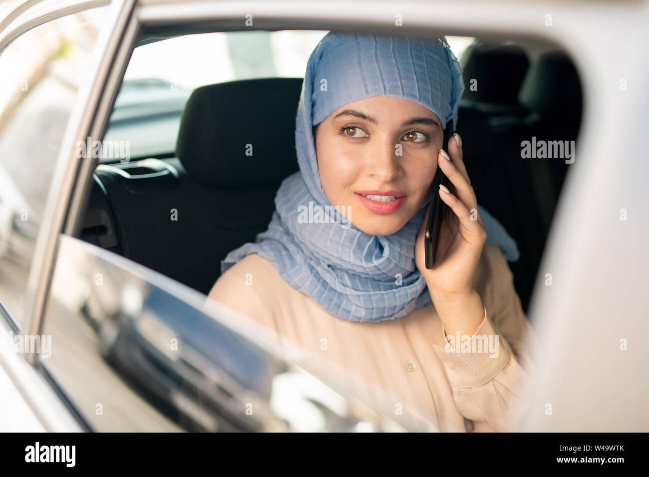 Hübsche junge islamische Geschäftsfrau im hijab sprechen auf dem Smartphone im Taxi Stockfoto