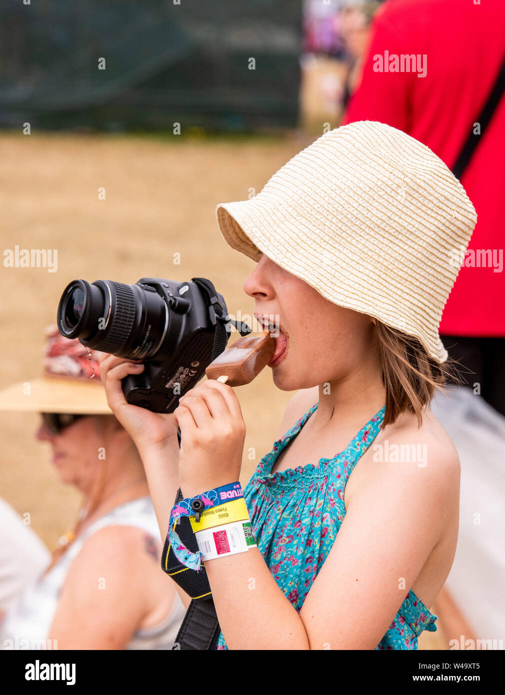 Junge Festival goer multitasking Fotos nehmen und Eis essen, Latitude Festival, henham Park, Suffolk, Großbritannien, Juli 2019 21. Stockfoto