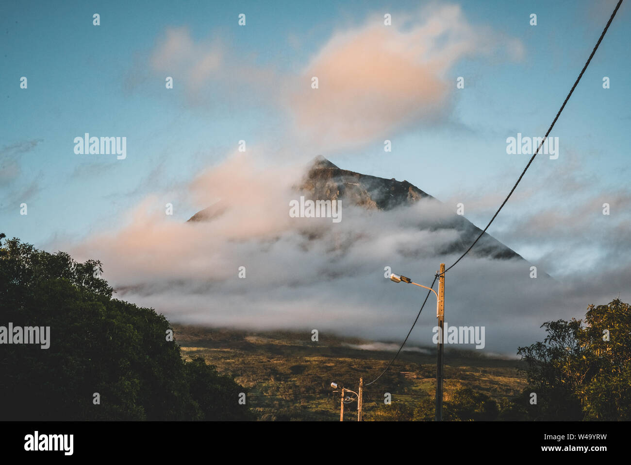 Den Berg Pico Vulkan westlichen Abhang von Ocean während mit Gipfel in Wolken gesehen nach Sonnenuntergang Sonnenaufgang mit rosa Himmel, von der Insel Faial, Azoren gesehen Stockfoto