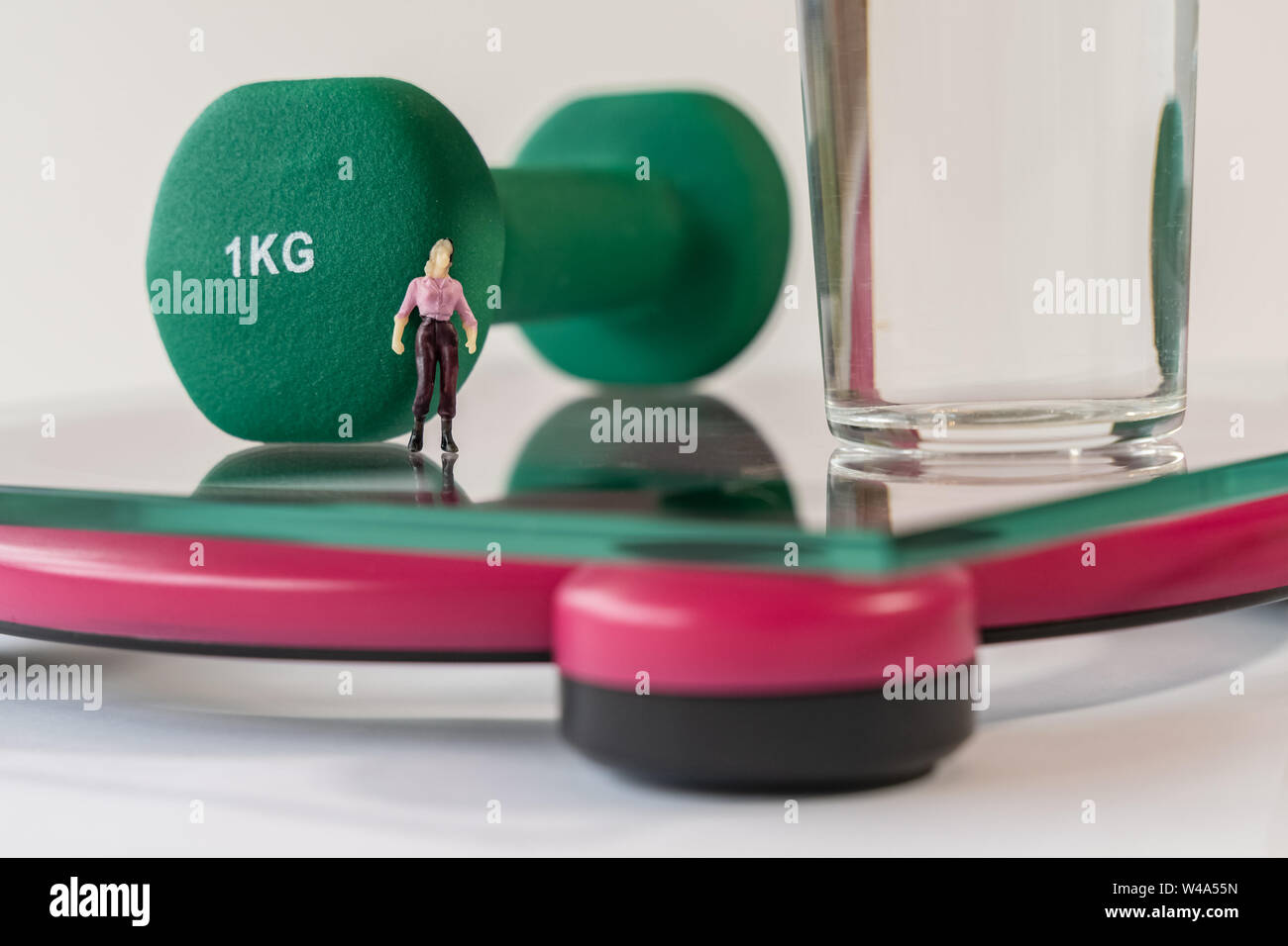 Miniatur Frau Abbildung auf die digitale elektronische Personenwaage, die für das Gewicht des menschlichen Körpers. Glas Wasser und Grün Hanteln in geringer Tiefe Stockfoto