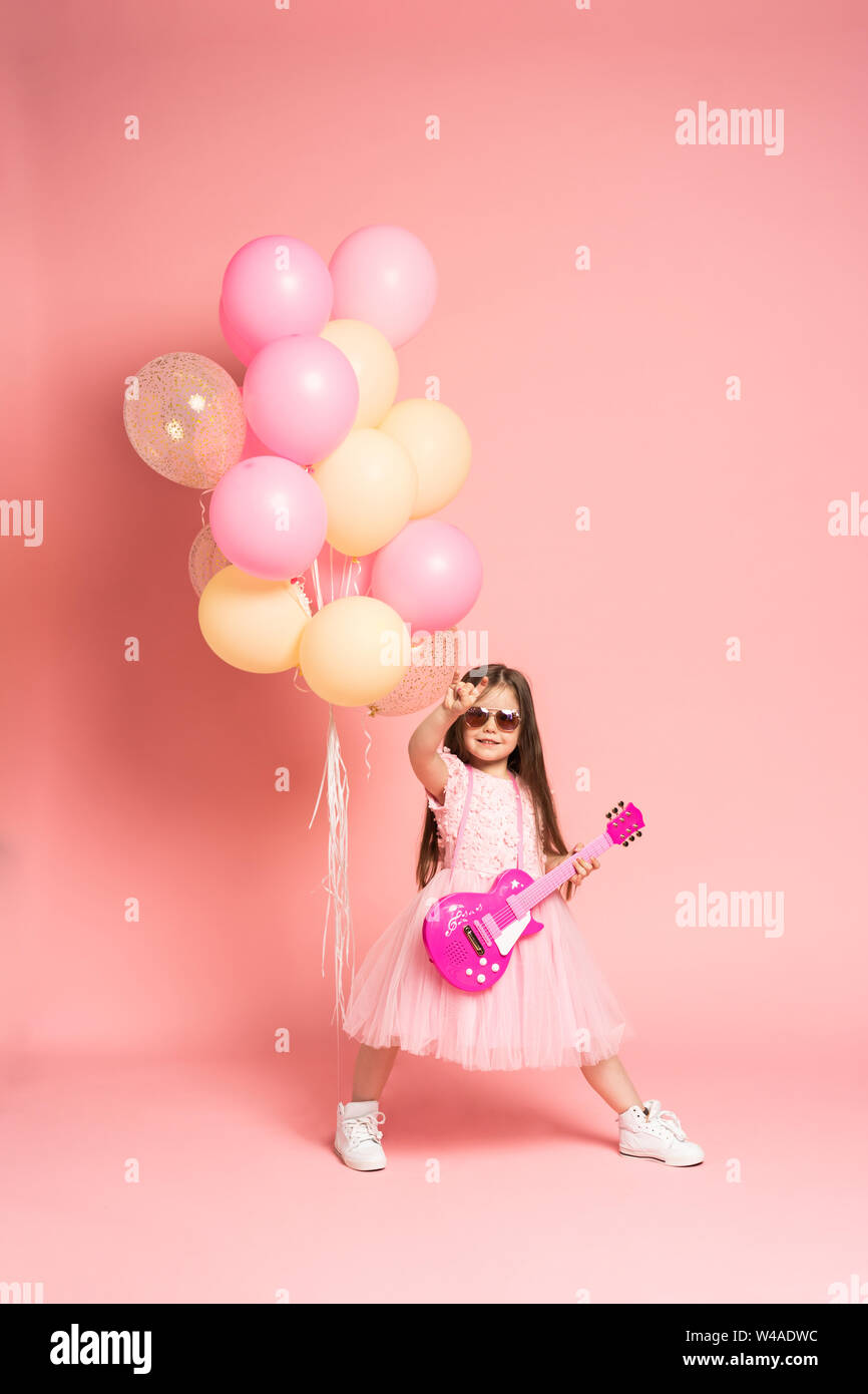 Lachen Mode Mädchen Spaß mit Gitarre auf rosa Hintergrund isoliert. Stockfoto