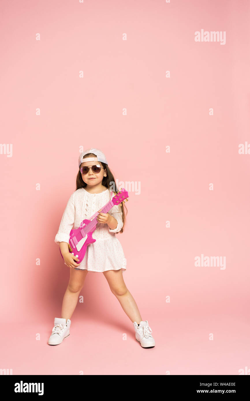 Lachen Mode Mädchen Spaß mit Gitarre auf rosa Hintergrund isoliert. Stockfoto