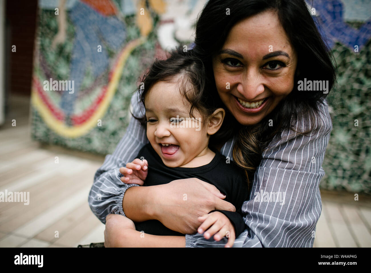 Mutter & Tochter umarmen lachend vor wandbild Stockfoto