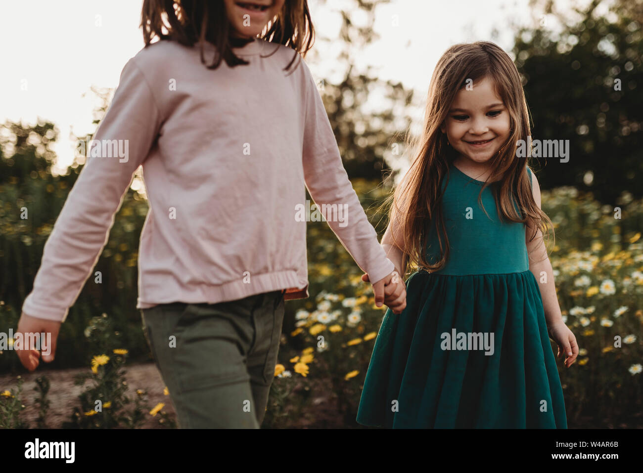 Lächelnde Schwestern zu Fuß durch ein Feld von Blumen im Frühling Stockfoto