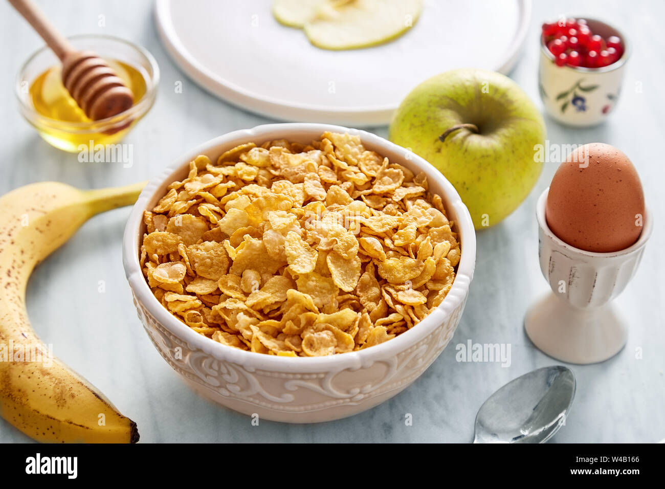 Cornflakes Schale, Apfel und Brot im Hintergrund. Gesundes Frühstück Stockfoto
