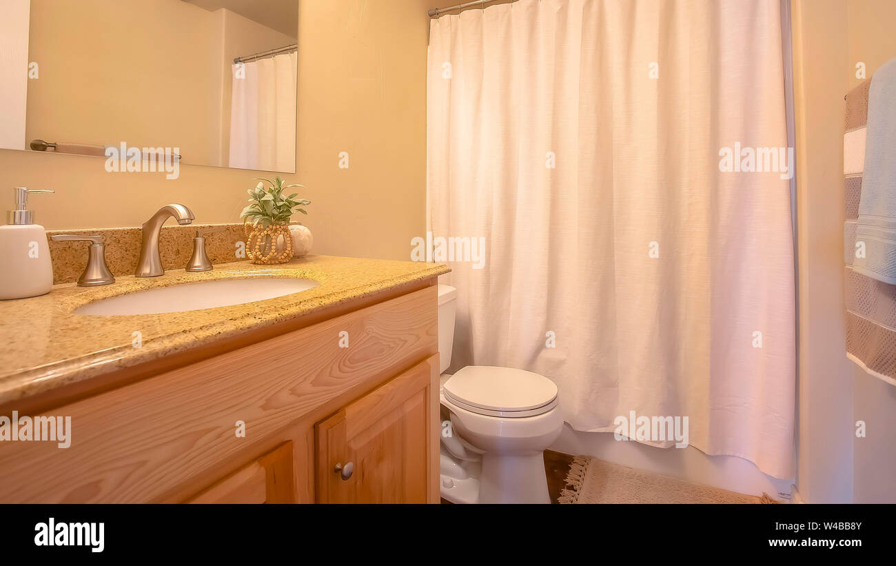 Panorama Toilette und Waschtisch im Badezimmer mit Handtuchwärmer Stange  und Spiegel an der Wand. Die Badewanne und Dusche befindet sich hinter  einem weißen Vorhang verdeckt Stockfotografie - Alamy