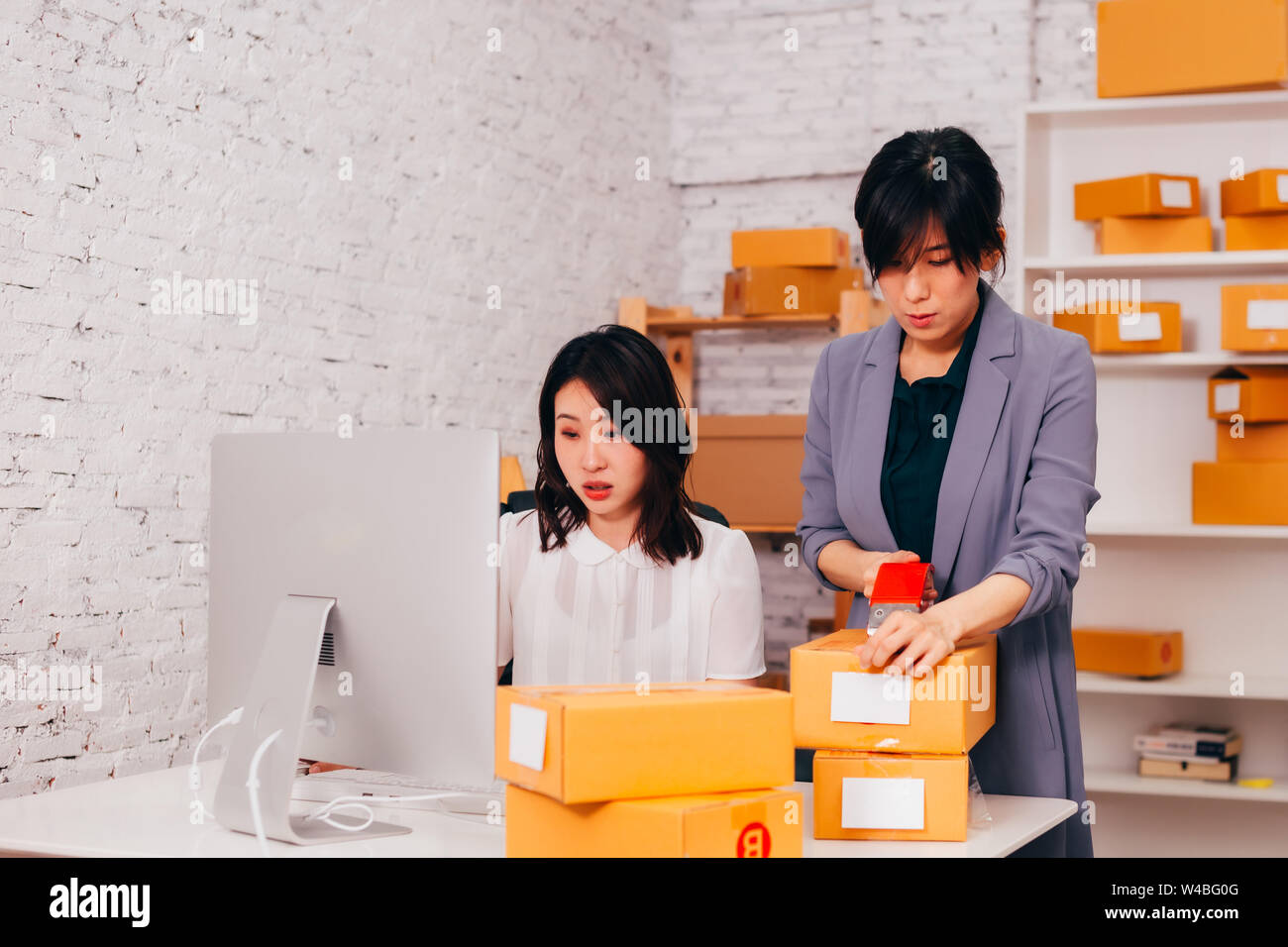 Zwei jungen asiatischen nach Fashion Business weiblichen Anbieter auf dem Handelsmarkt im Amt an den on-line-Unternehmen arbeiten mit Paketen von Kleidung geliefert werden Stockfoto