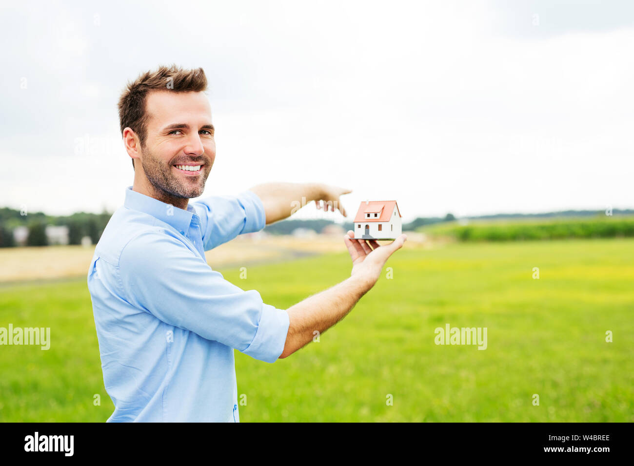 Glückliche Menschen mit Miniatur zeigt auf Feld für neues Haus Stockfoto