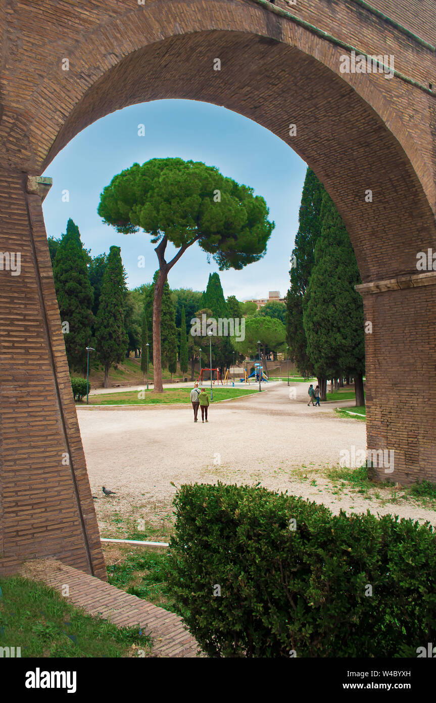 Leute, die in einem Park in der Nähe von Castel Sant'Angelo Schloss unter grünen Bäumen und Büschen unter dramatischen bewölkt herbst himmel. Natürliche Frame von einem Steinbogen Stockfoto