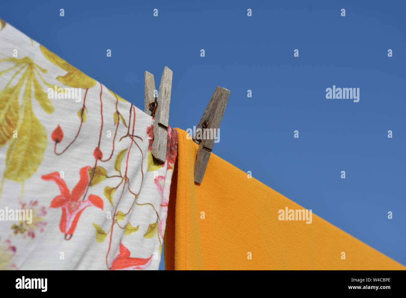 Wäsche auf dem Trockenen sitzen im Freien an einem heißen sonnigen Tag. Nahaufnahme, Detail der bunten Hemden und Wäscheklammern gegen den blauen Himmel Hintergrund mit Kopie sp Stockfoto