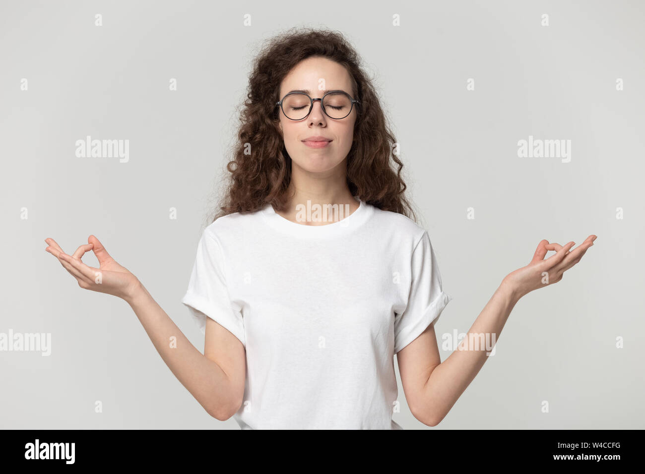 Ruhige junge Frau Meditation Pose auf Grau studio Hintergrund Stockfoto