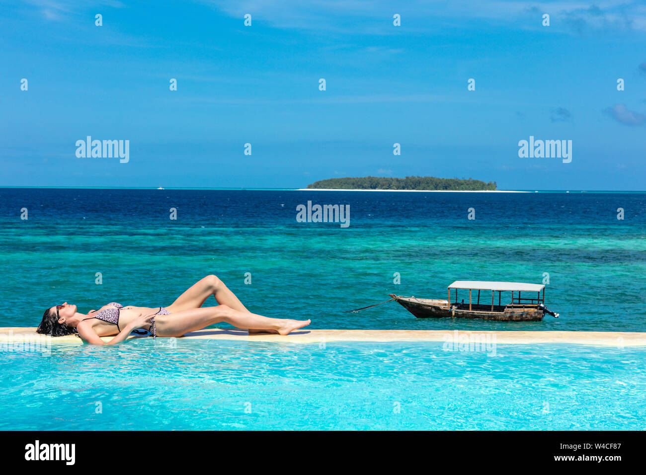 Eine kaukasische Frau genießen Ferien Sonnenbaden auf ein Infinity Pool direkt am Meer, mit Blick auf den Ozean idian Muyuni in Unguja aka Insel Sansibar Tansania Ostafrika Stockfoto