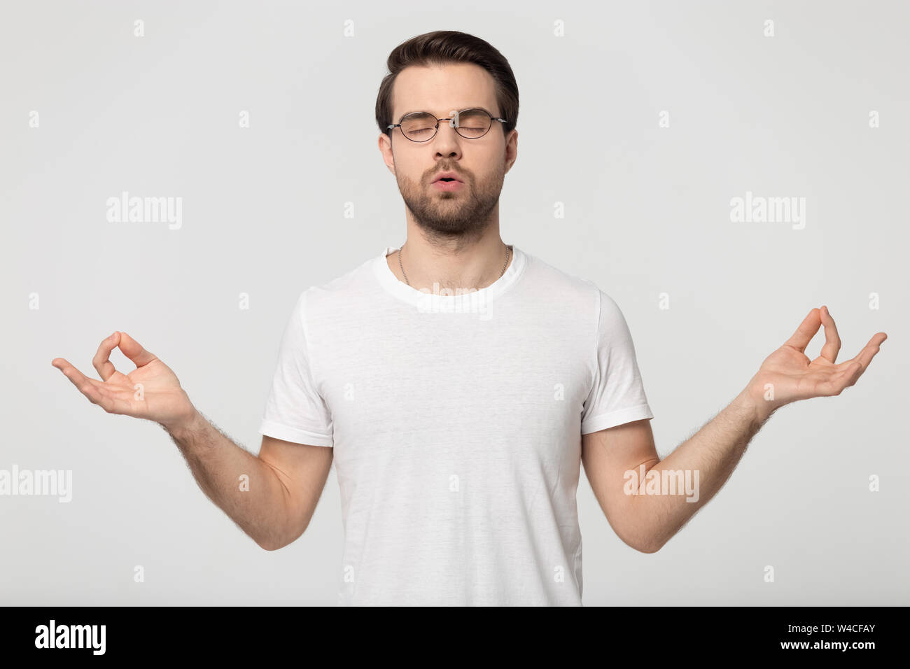 Junger Mann in Gläser zu tun atmen Übungen isoliert auf Grau Stockfoto