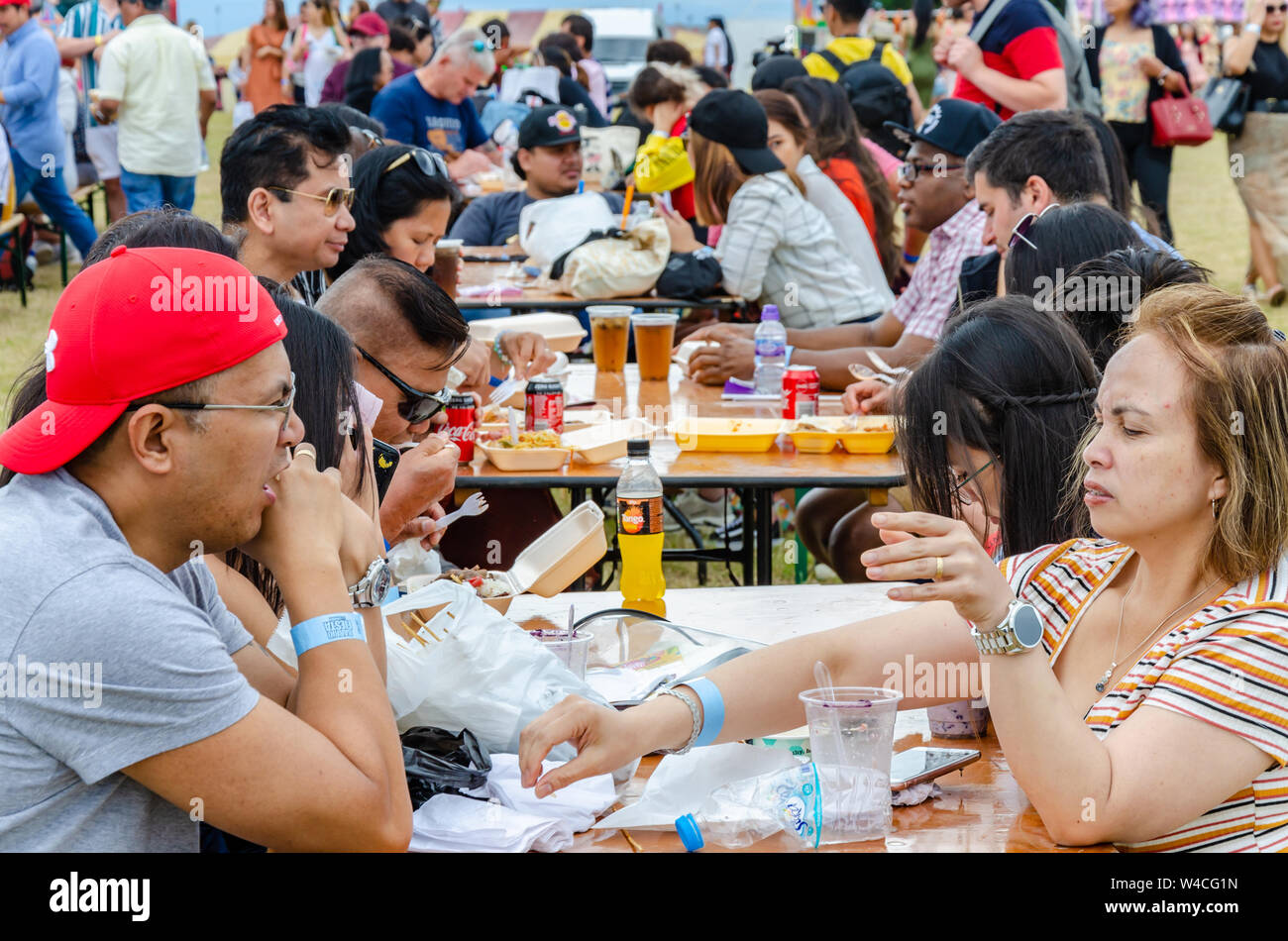 Die Leute sitzen Außen am Gestell Tisch und essen Essen gekauft Form geht im Barrio Fiesta in London. Stockfoto