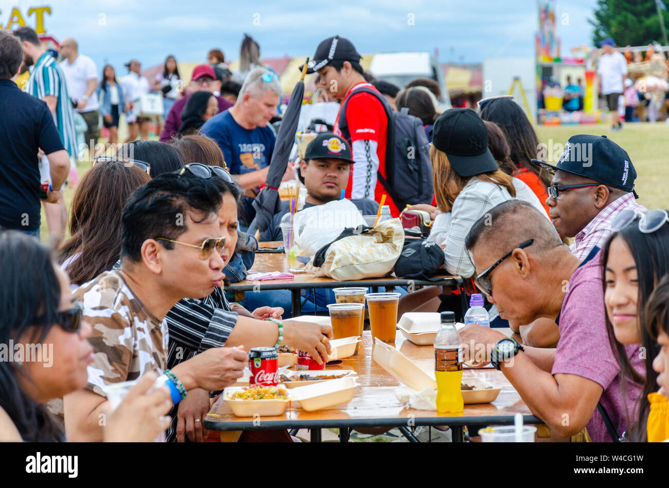 Die Leute sitzen Außen am Gestell Tisch und essen Essen gekauft Form geht im Barrio Fiesta in London. Stockfoto