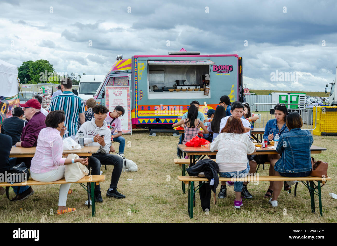 Eine mobile Gastronomie van verkauft Filipino Street Food. Die Leute sitzen an Holztischen im Barrio Fiesta auf London Essen Stockfoto