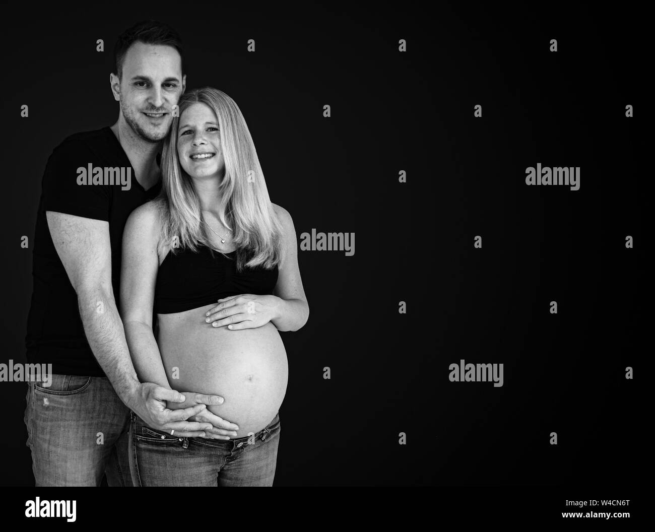 Der Mensch und seine schöne schwangere Frau sind, umarmen und lächelnd Stockfoto