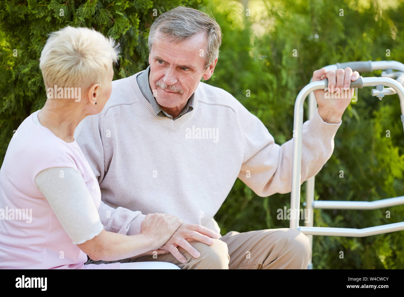 Volle Länge Portrait von älteren Mann lehnte sich auf Wanderer sitzt auf der Bank im Park mit fürsorglichen Krankenschwester oder Frau, Kopie Raum Stockfoto
