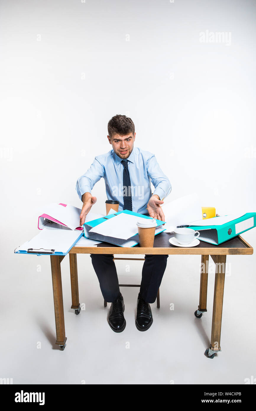 Der junge Mann hat eine komplette Verwirrung am Arbeitsplatz, er kann nicht organisieren seinen Platz und wichtige Dokumente finden. Konzept der Probleme im Büro, Business, Werbung, alltägliche Probleme. Stockfoto