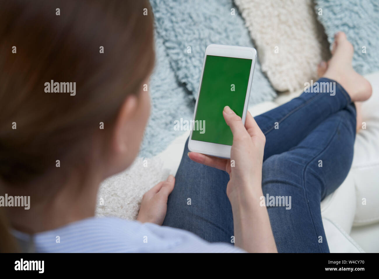 Blick über die Schulter der Frau liegt auf einem Sofa mit Green Screen Handy zu Hause Stockfoto