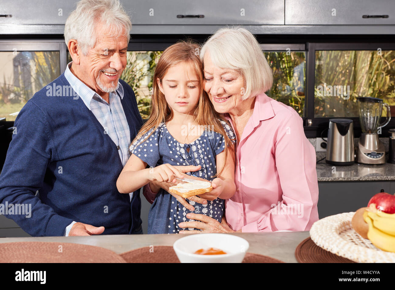 Großeltern helfen, ihre Enkelin bestreichen Brot am Morgen in der Küche Stockfoto