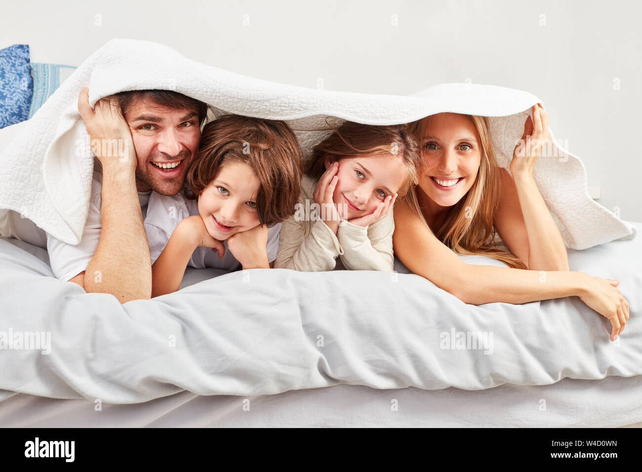 Eltern und zwei Kinder im Schlafzimmer unter die Abdeckungen am Morgen ausblenden Stockfoto