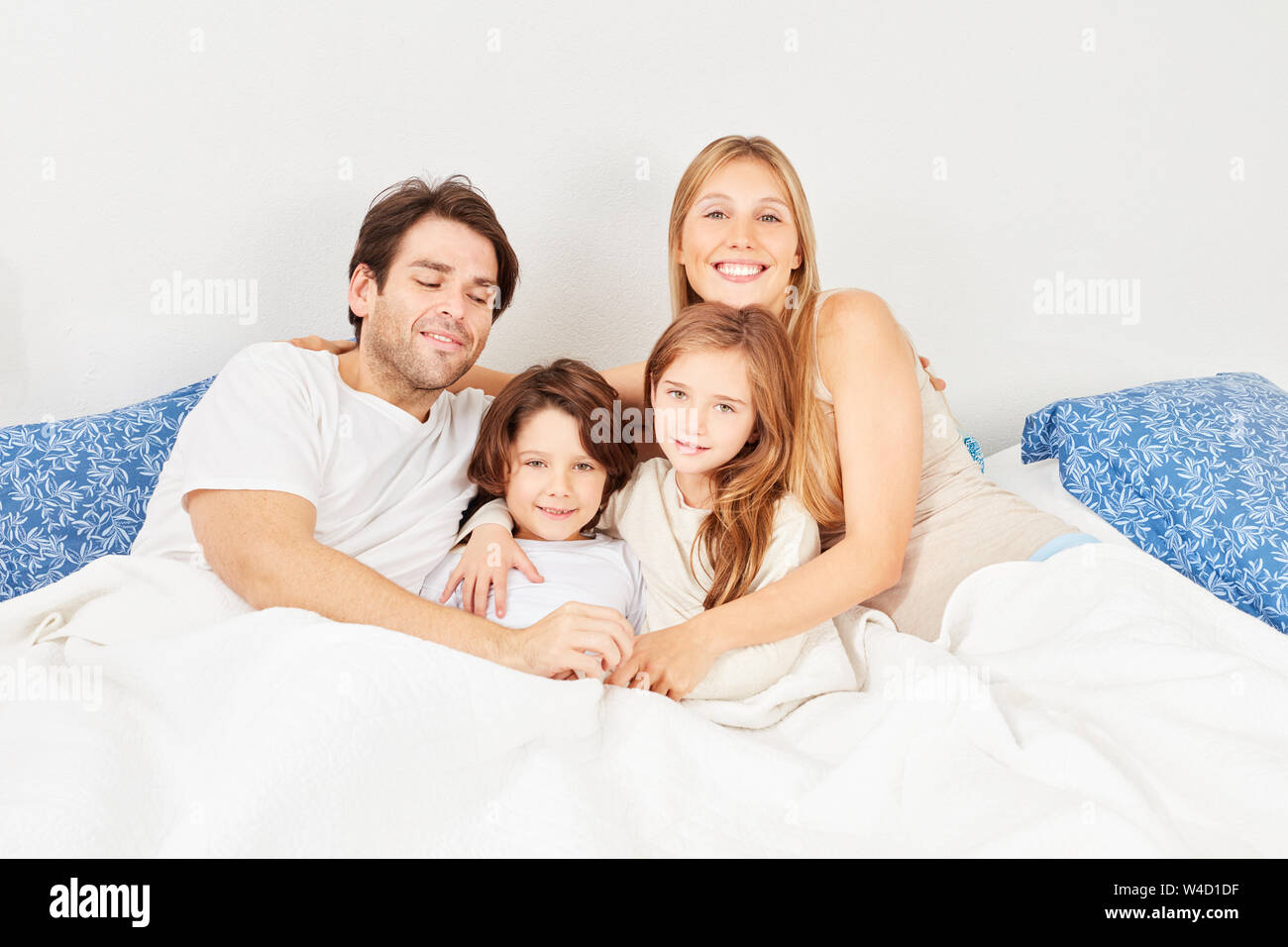 Glückliche junge Eltern und zwei Kindern im Schlafanzug zusammen kuscheln im Bett Stockfoto