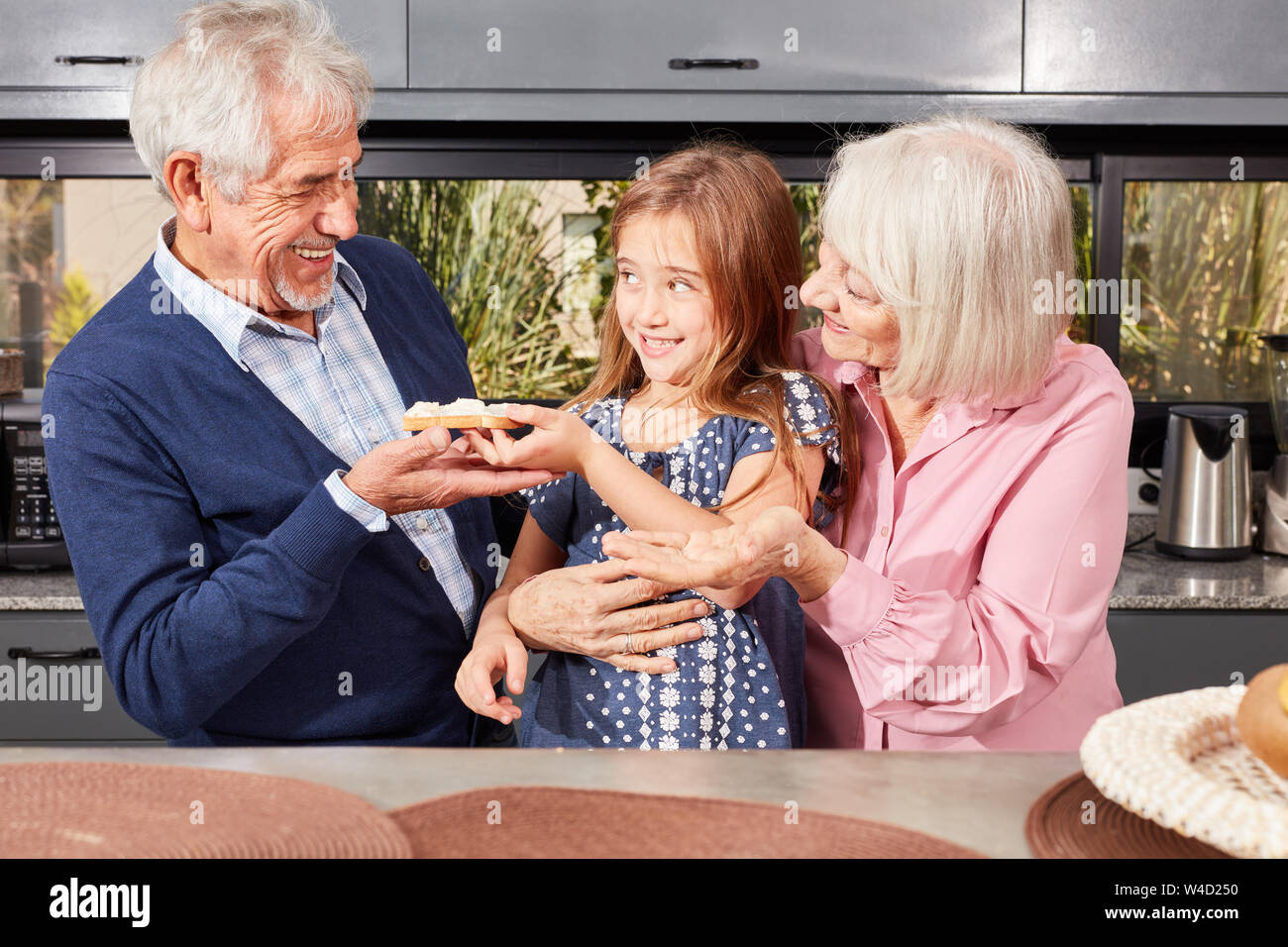 Enkelin teilt ihr Brot mit Großvater beim Frühstück am Morgen in der Küche Stockfoto