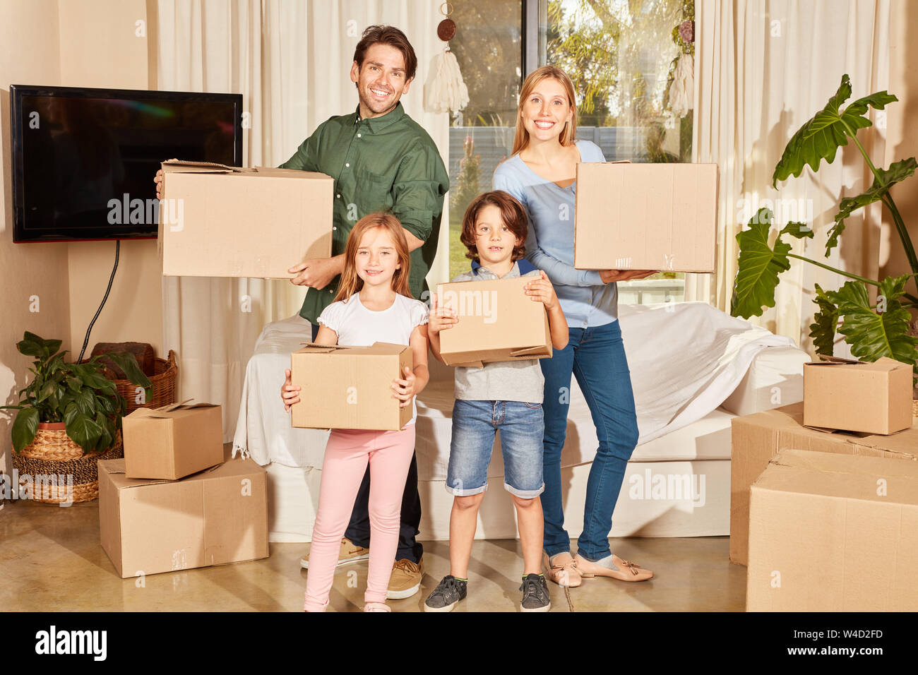 Glückliche Familie mit zwei Kindern steht mit Kisten in der neuen Wohnung Stockfoto